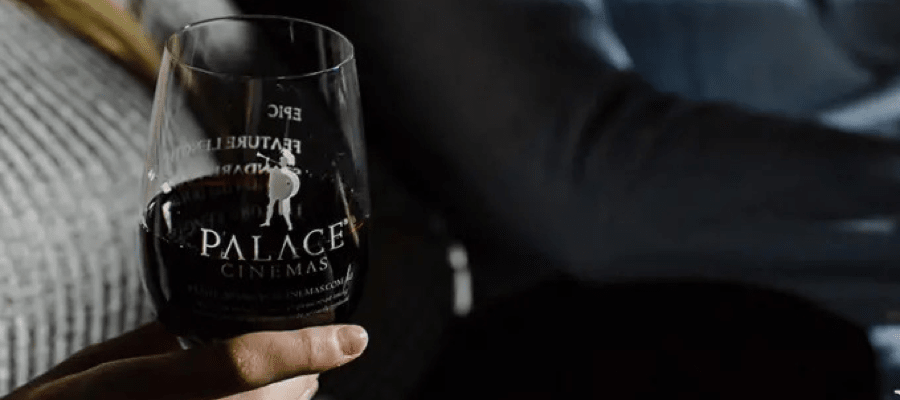 Close up of someone holding a logo etched wine glass, sitting at a Palace Cinema